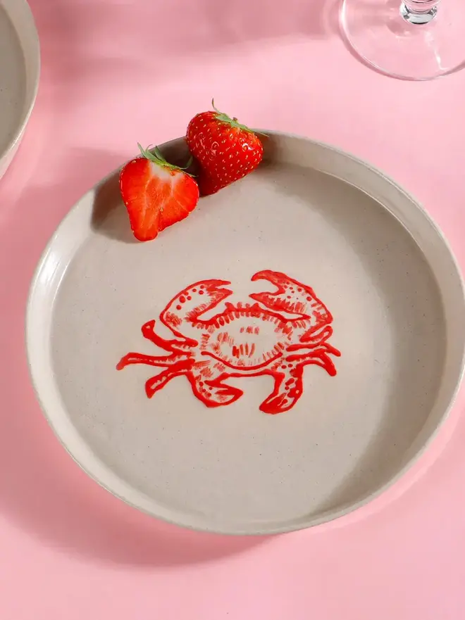 Handmade Ceramic Side Plate With A Red Crab Design, a white side plate with a red crab on a pink table. 