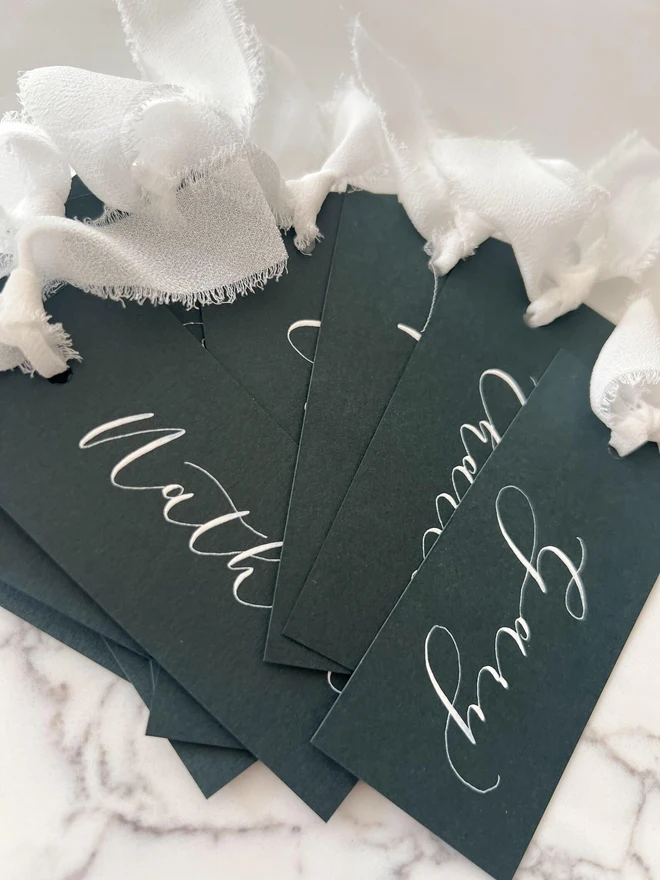 Personalised Calligraphy Wedding Forest Green Place Cards, grouped together with white ribbon. 