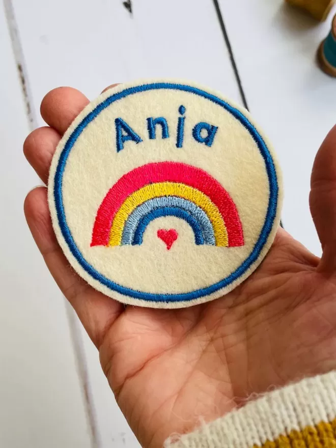 An embroidered rainbow name patch being held in a hand to show the scale.