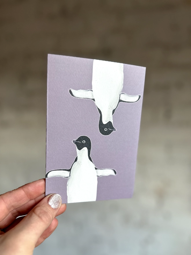 a purple greetings card featuring two illustrations of a penguin