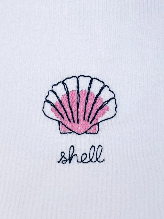     White T-shirt embroidered with pink shell motif and the word “shell”