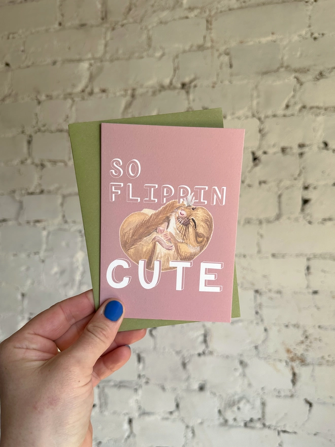 a dusty pink greetings card featuring an illustration of a sleeping mouse with the text “so flippin cute” with a green envelope