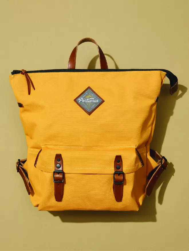 Yellow zip top Shortwood backpack with brown leather trim on a plain taupe background.