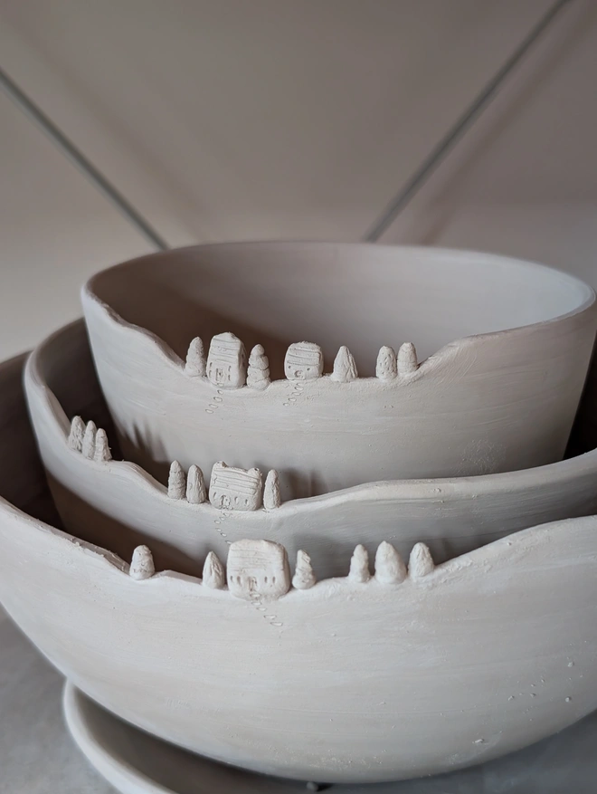Handmade ceramic clay nesting bowls with tiny house and tree details on the rim of all three bowls nesting inside each other 