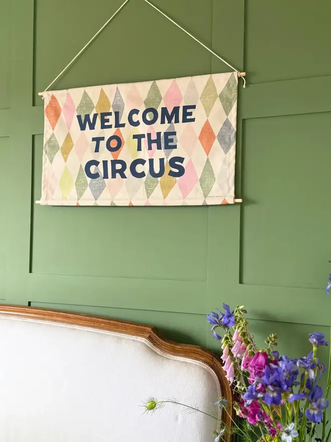 'Welcome To The Circus' Cotton Wall Hanging, hanging on a green wall. 