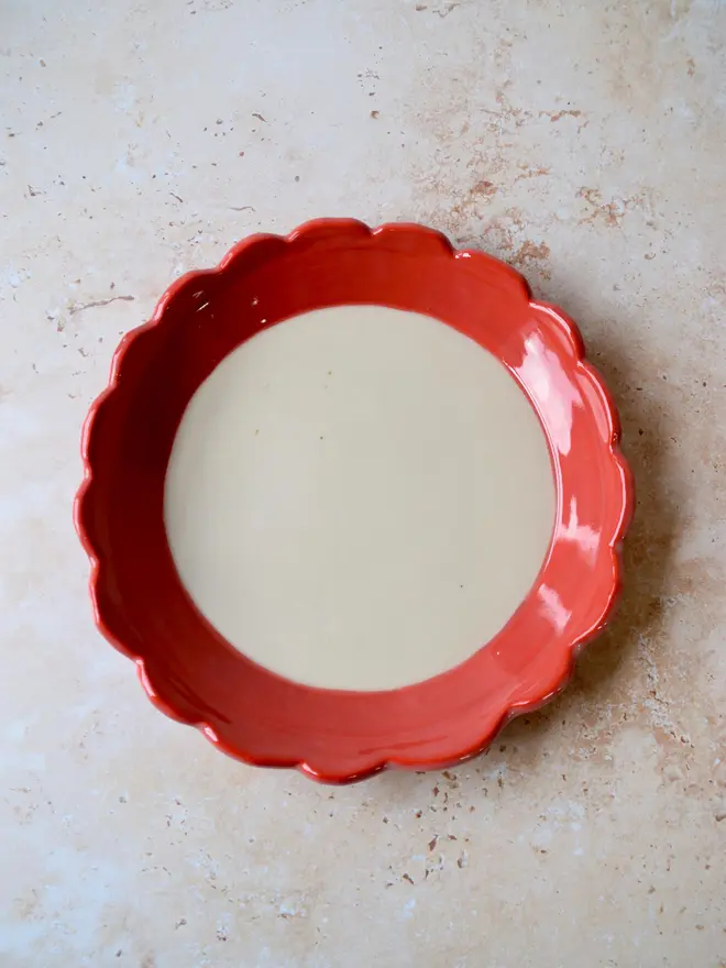 Handmade ceramic plate with red scalloped rim — full view from above