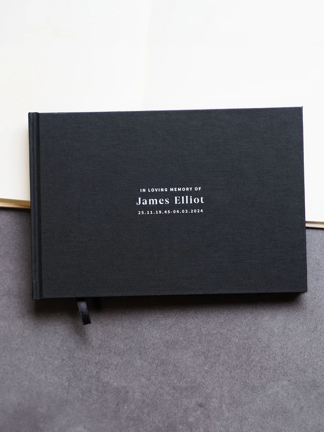 a black linen condolence book personalised with the name James Holt
