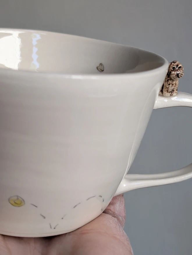 white cup with a tiny brown cockapoo on the handle of the mug with an illustration of a bouncing tennis ball and hearts