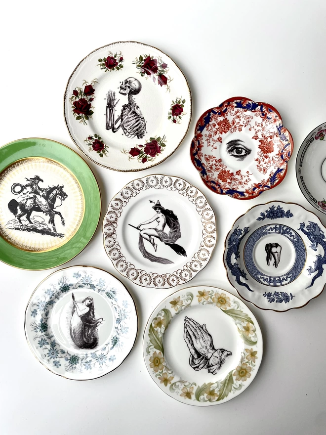 an eclectic collection of vintage plates hung together on a white wall, each plate is different with patterned or gold borders and vintage images in their centres