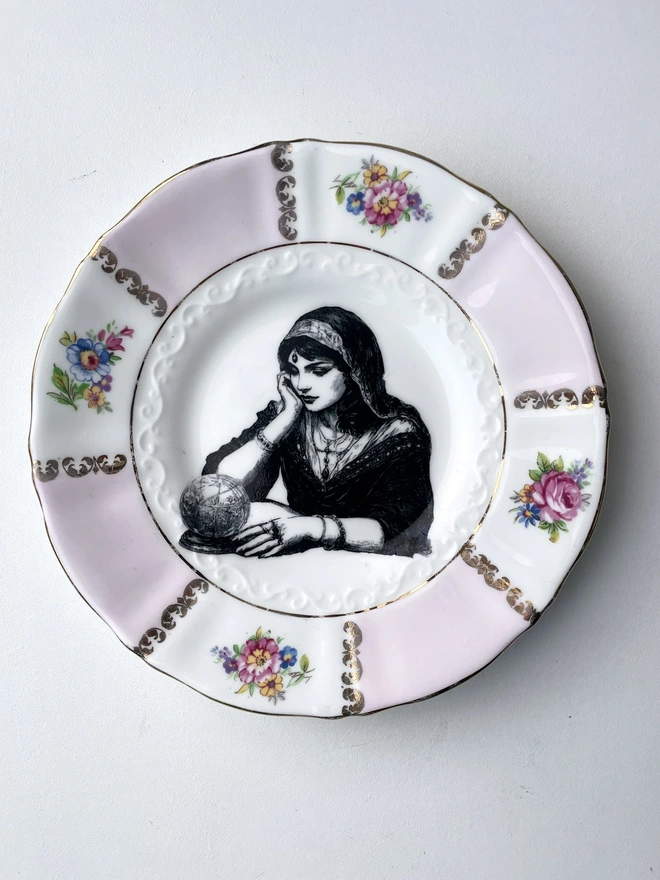 a vintage ornate plate with a pink floral border detail, in the centre i have printed a vintage black and white illustration of a pretty fortune teller reading a crystal ball