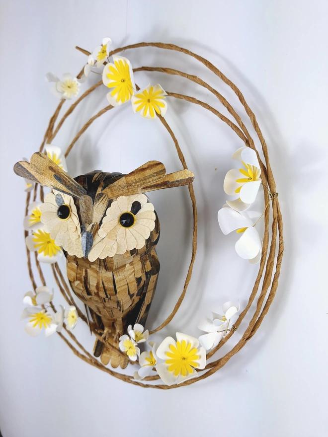 Handmade paper sculpture of a long eared owl, perched on a spring wreath of white and yellow tree blossom flowers