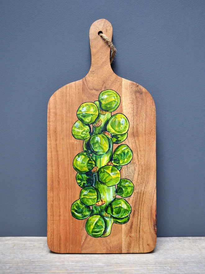 A wooden serving board with a handpainted design of Brussels sprouts