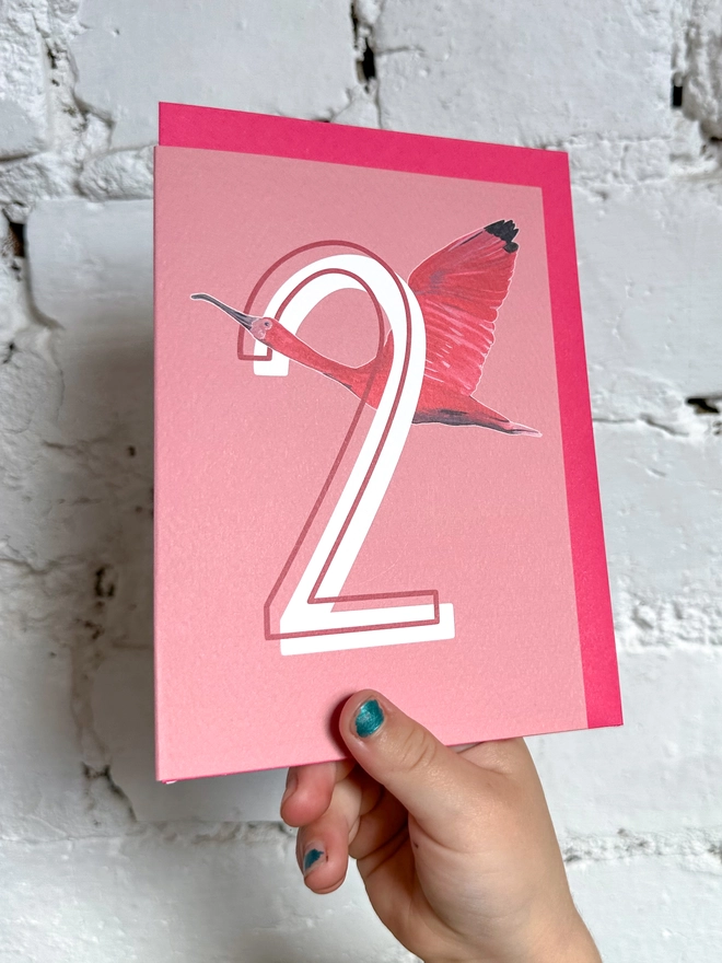 a pink card with a big white number 2 and an illustration of a scarlet ibis with a neon pink envelope