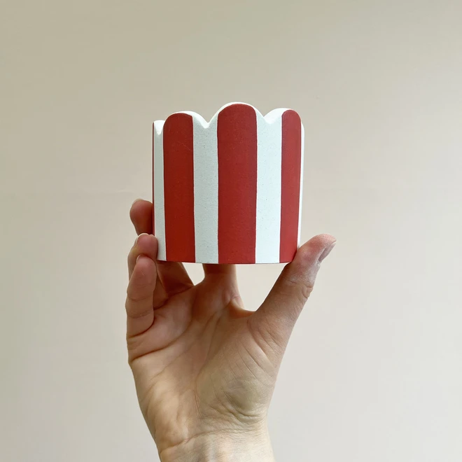 Small Scalloped Coral and white striped pot held against a plain background.