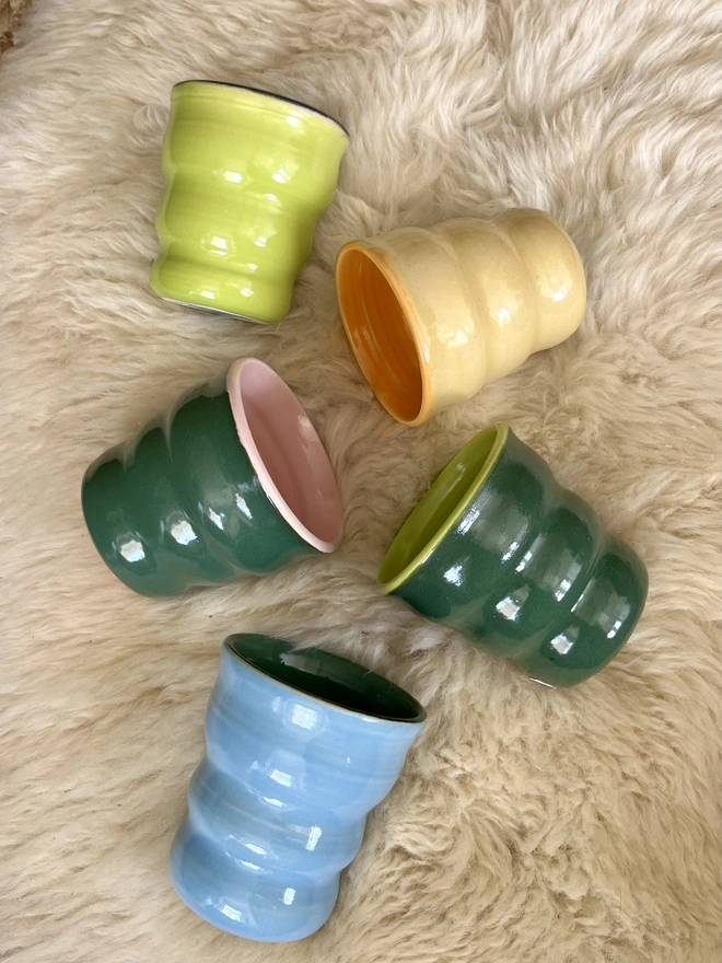 a selection of colourful ceramic tumblers on a sheepskin rug