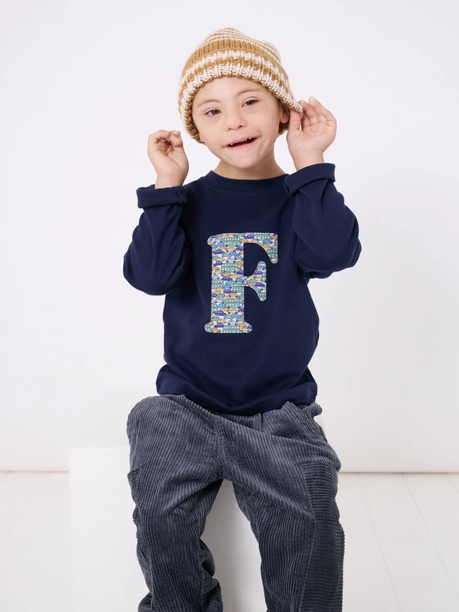 A navy cotton long sleeve t-shirt appliquéd with an initial in a vintage cars and busses Liberty print, worn by a 4 year old boy