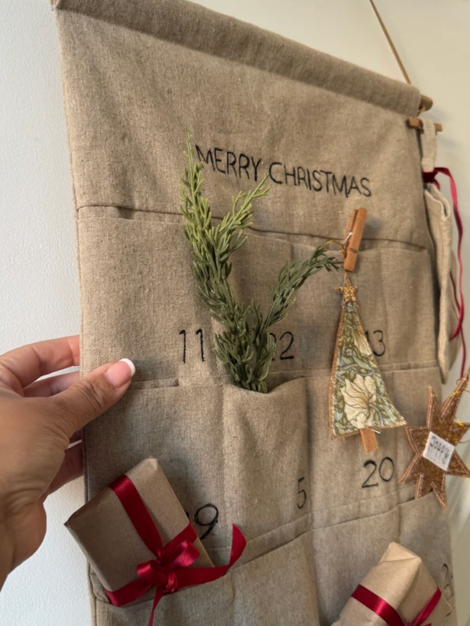 Linen Embroidered Advent Calendar. An advent calendar hanging on a wall, filled with Christmas treats.
