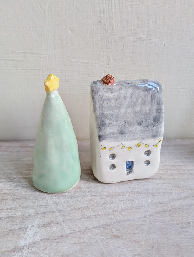 grey tiny pottery house with a tiny robin bird on top with a ceramic Christmas tree with a star on top