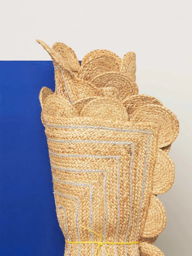 Jute mats with scalloped edging rolled together and displayed n front of a bright blue wall