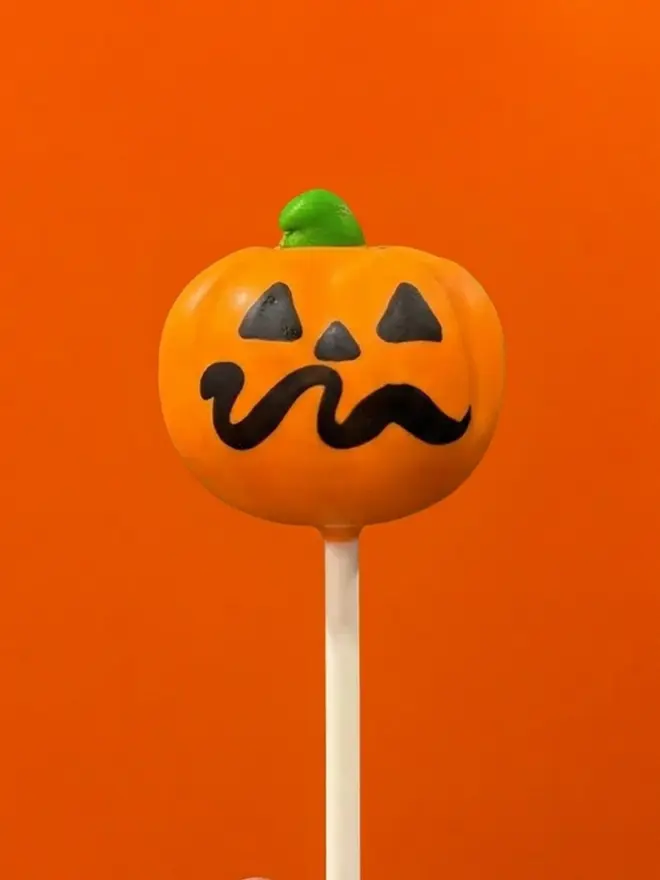 Pumpkin cake pop on a white stick against a bright orange background