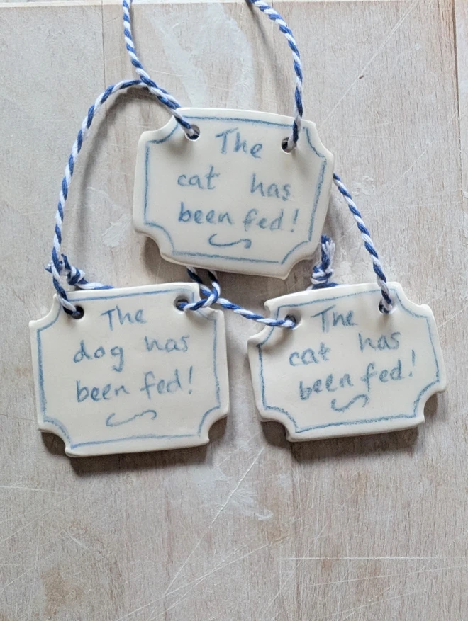 the cat or dog has been fed sign in blue and white ceramic hanging decoration