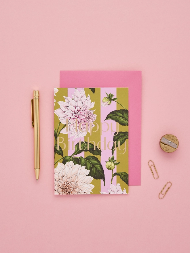 happy birthday card with gold foil wording and illustrated Dahlia flower on a green and pink stripes base and a hot pink envelope