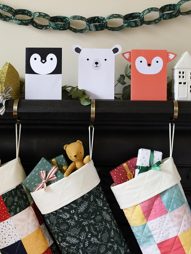 Three animal shaped greetings cards stand on a black mantlepiece where two patchwork stockings are hanging from.