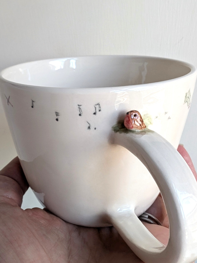 ceramic cup with a tiny pottery robin on the handle with musical notes and tiny bird prints