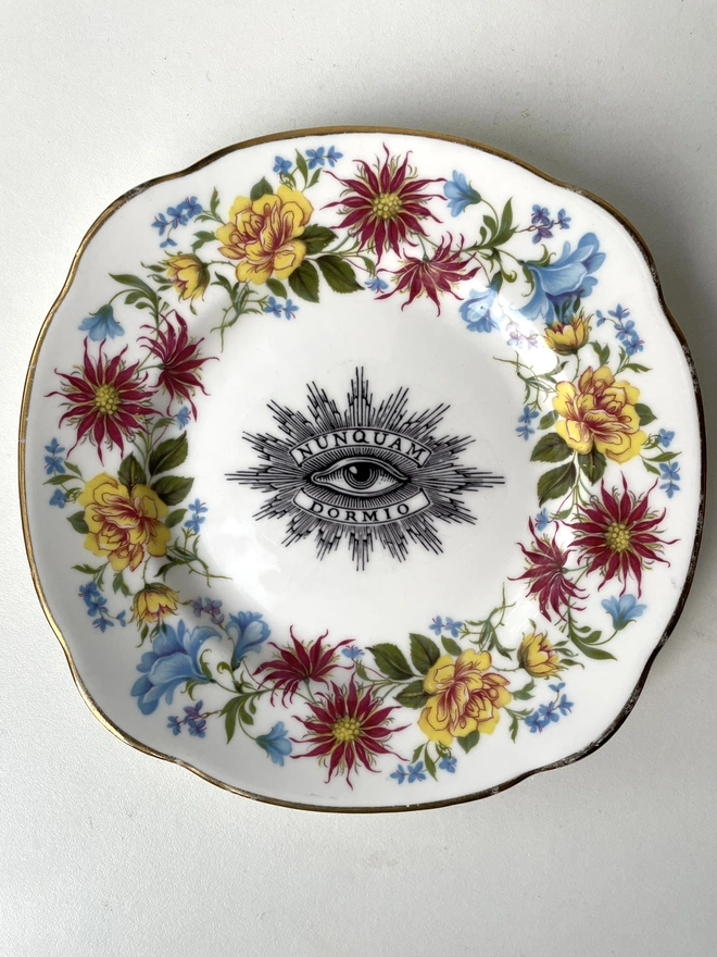 a very ornate vintage plate with patterned border, in the centre is a vintage black and white illustration of an eye