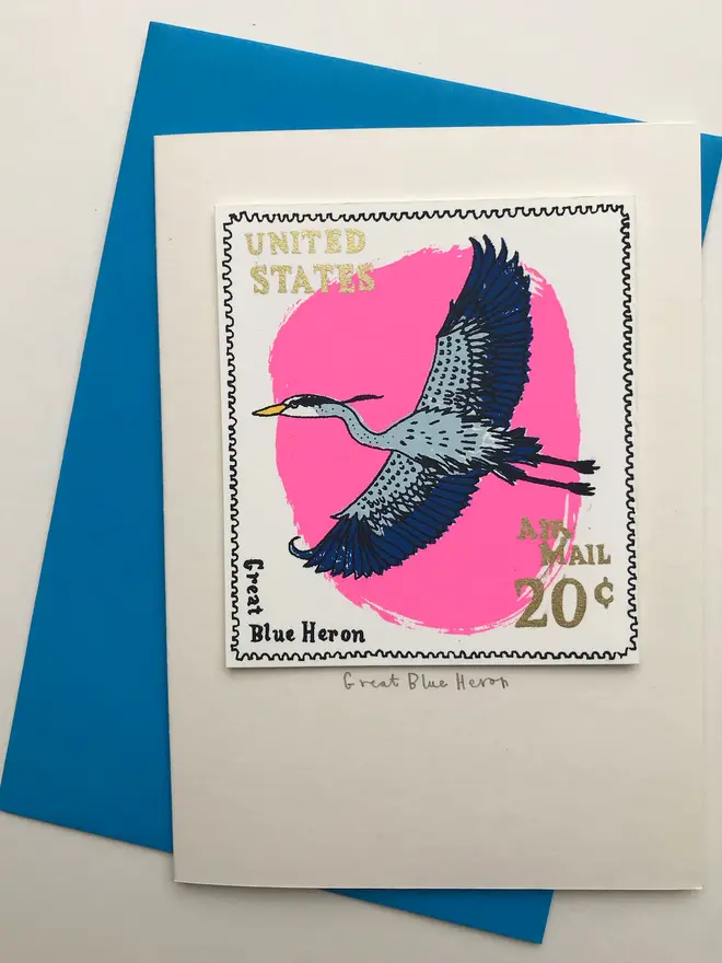 Bird Stamp Card Great Blue Heron/ American, a white card with a colourful bird design in the centre against a blue envelope on a white surface. 