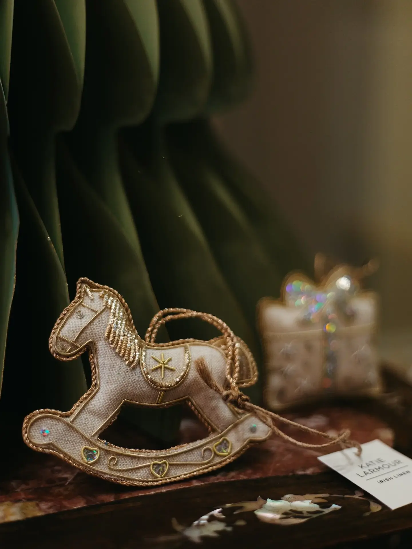 embroidered linen rocking horse decoration. rocking horse hanging ornament pictured on dark wooden shelf.