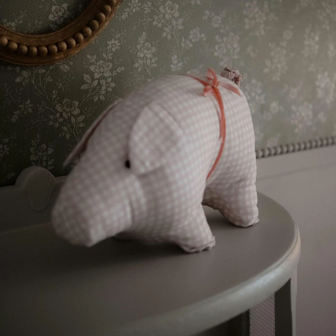 Cotton Pig Pillow Ornament, a pink pillow ornament sitting on a table in a bedroom. 