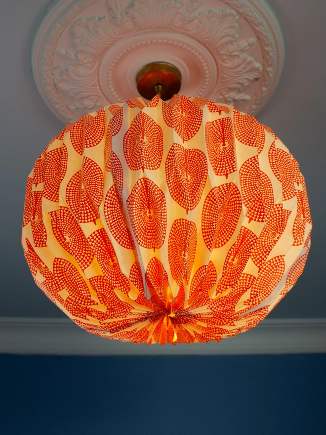 A vintage-inspired paper lampshade with a bold geometric pattern adds a touch of retro flair to a room with a blue wall and ornate ceiling. The lampshade is made from folded paper, creating a unique and eye-catching design.