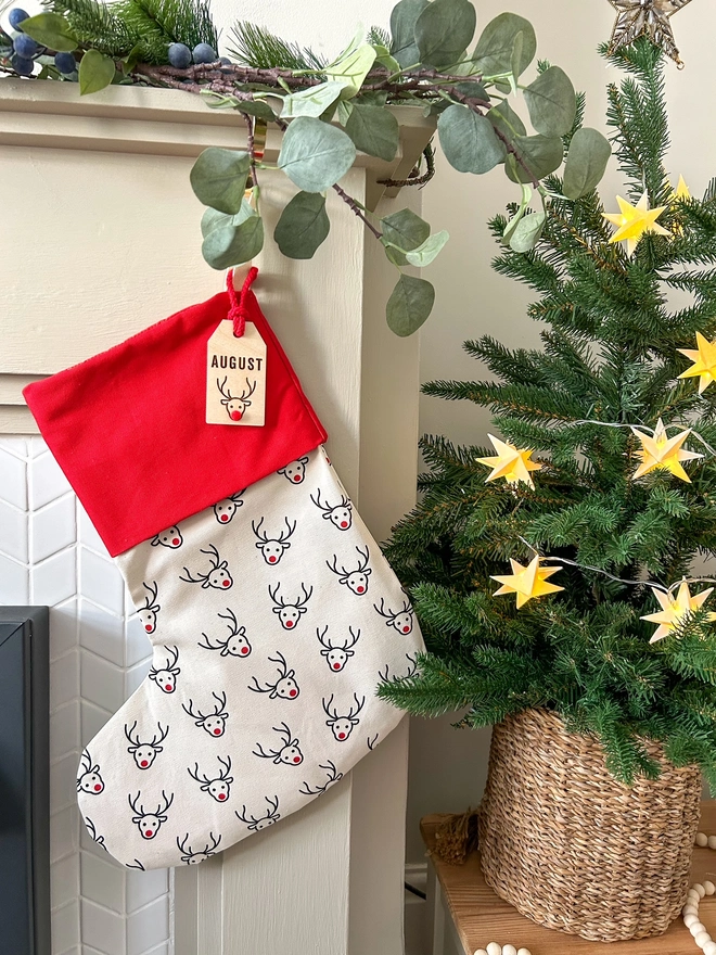 Reindeer Print Christmas Stocking with Lasercut personalised tag hanging on the fireplace next to a Christmas Tree