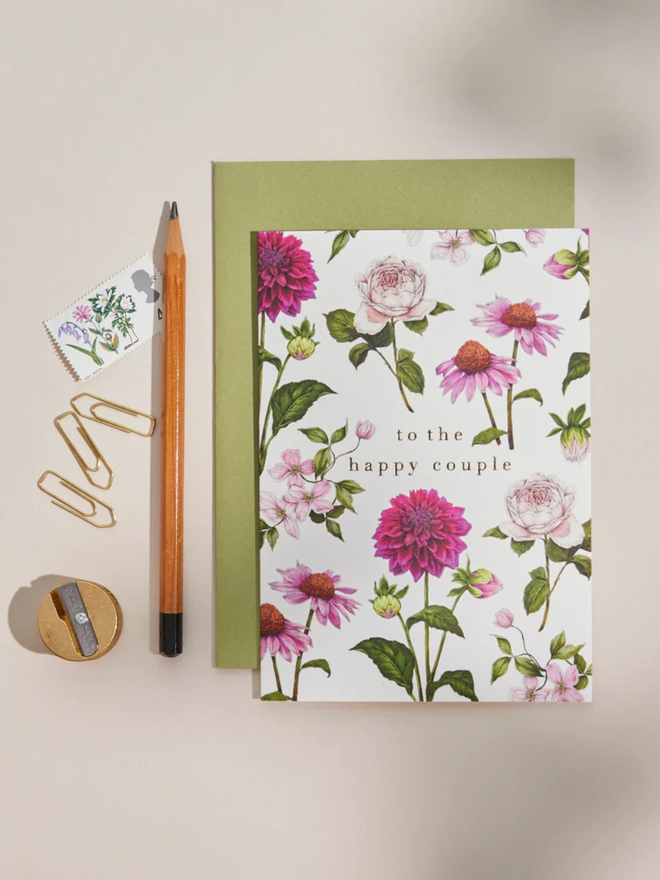 'to the happy couple' illustrated floral card. a white floral card and green envelope photographed against a plain background.