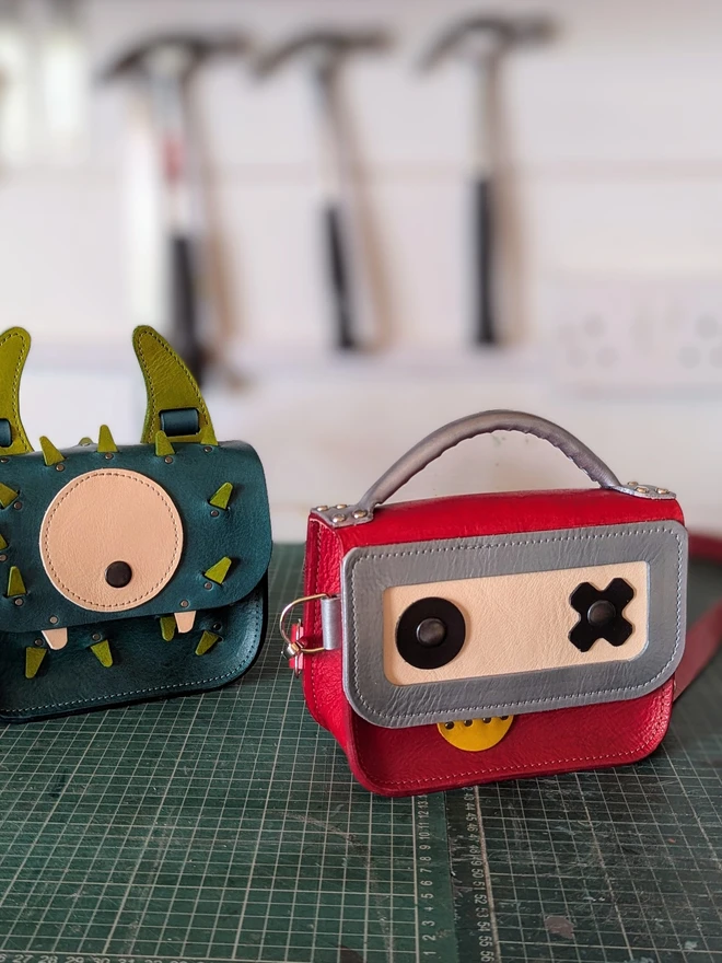 Red robot cross- body bag pictured on workshop bench, viewed from the front.