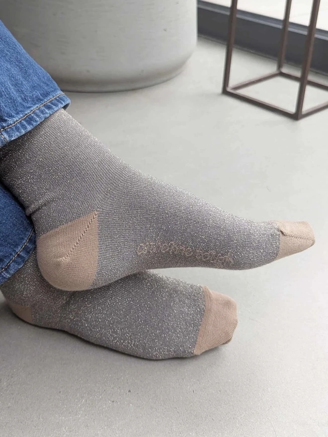 Women's Glitter Organic Cotten Ankle Socks, a woman wearing a pair of colourful patterned socks above a decorated surface. 