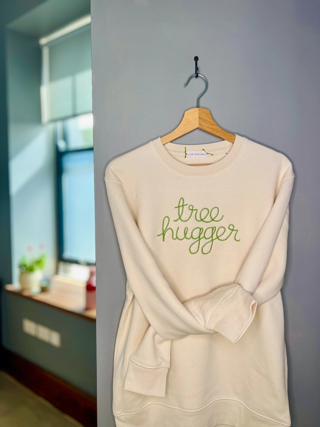 A natural sweatshirt on a hanger embroidered with tree hugger