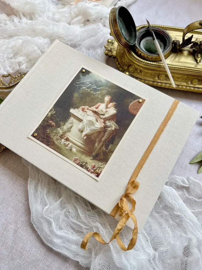 Luxury fabric printed wedding guest book featuring an images of lovers from an 18th century rococo work of art. Linen covered book finished with ribbon