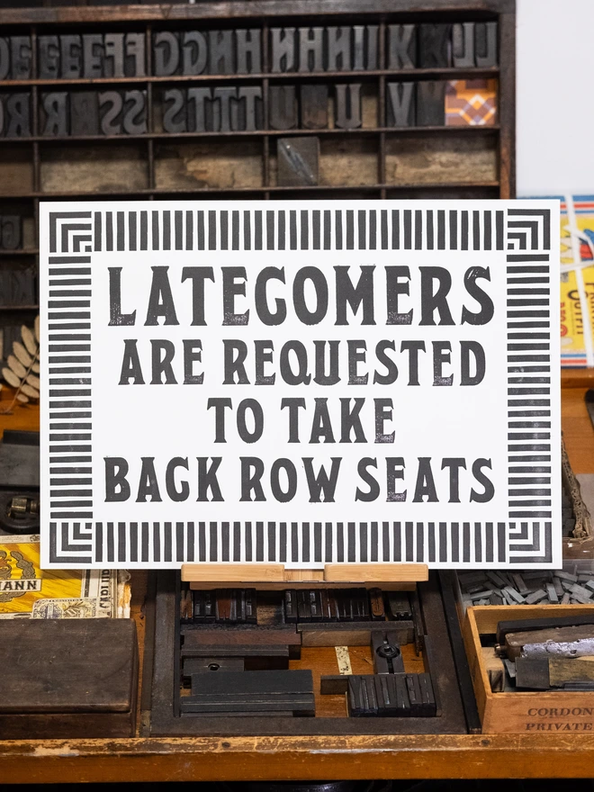 A3 letterpress print with vintage serif block font text design "Latecomers are requested to take back row seats" surrounded by vintage art-deco style border of parallel lines