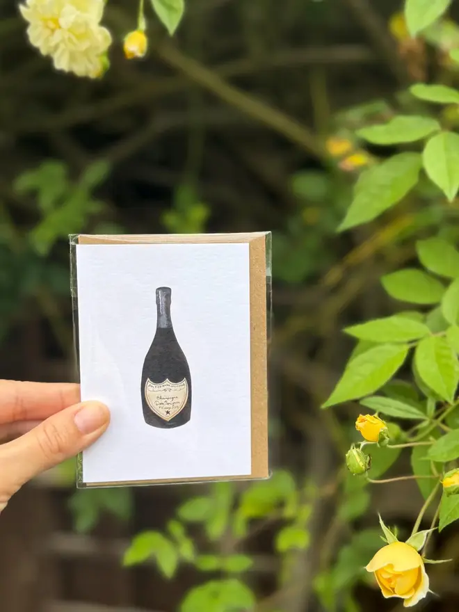 champagne bottle illustrated mini cards (pack of 3). card held against rosebush backdrop.
