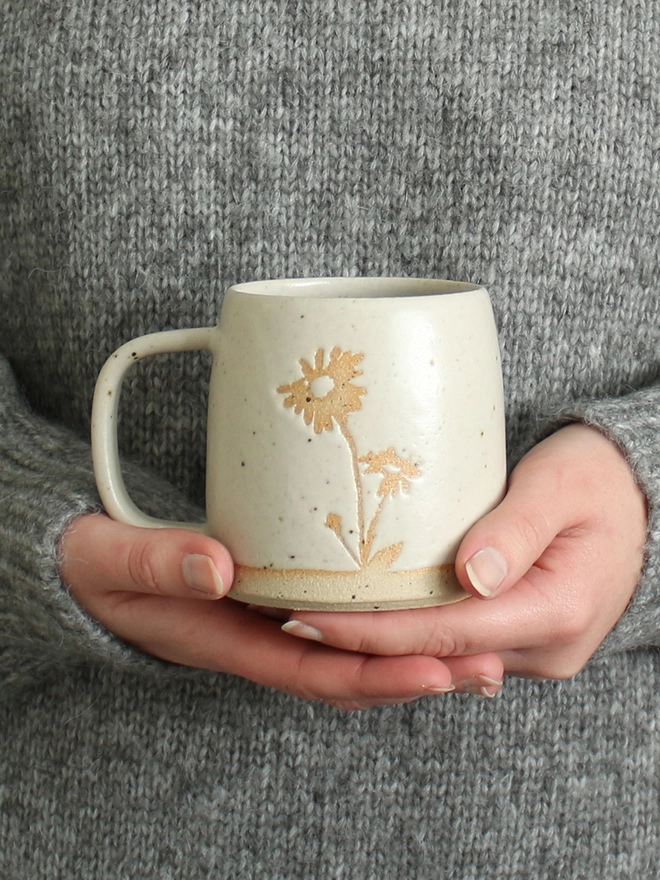 Hands holding white stoneware mug with an illustration of an Aster flower