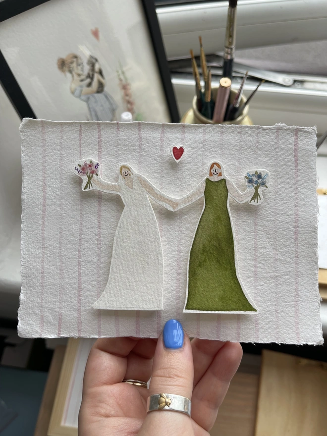 a illustration of a bride and bridesmaid holding hands and each holding a bouquet of flowers. mounted onto handmade paper as an A6 gift.