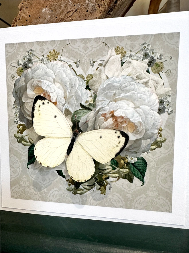 A handmade Diamond Wedding aA vintage floral heart design featuring white roses and on a taupe background. The recipients initials are hand written on the front of card and hand signed, A white 3D papercut butterfly sits on the heart and wings can be folded out for display.