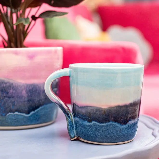 Landscape Standard Mug, a colourful mug placed on a desk. It is accompanied by flowers. 