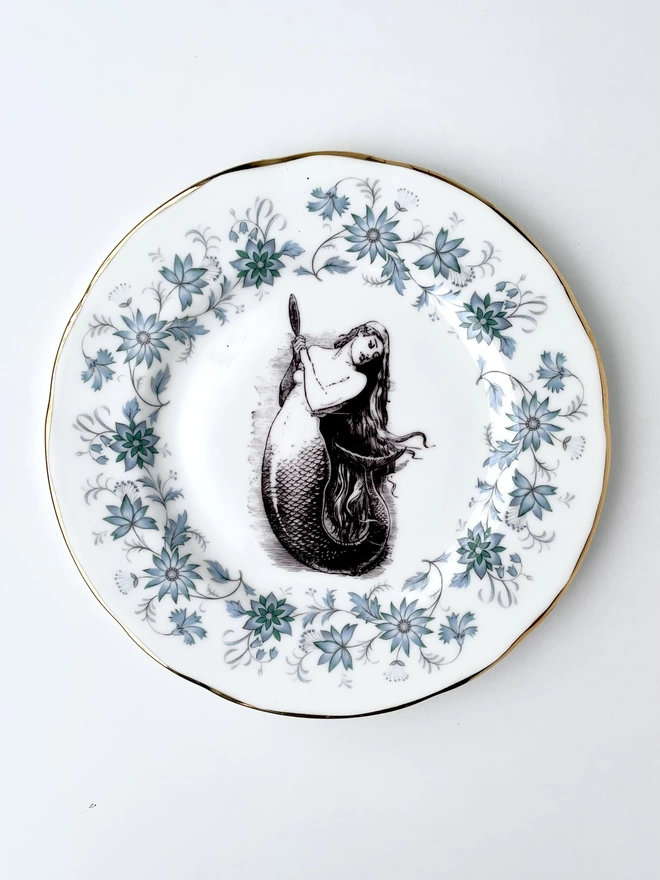 vintage plate with an ornate border, with a printed vintage illustration of a mermaid in the middle 