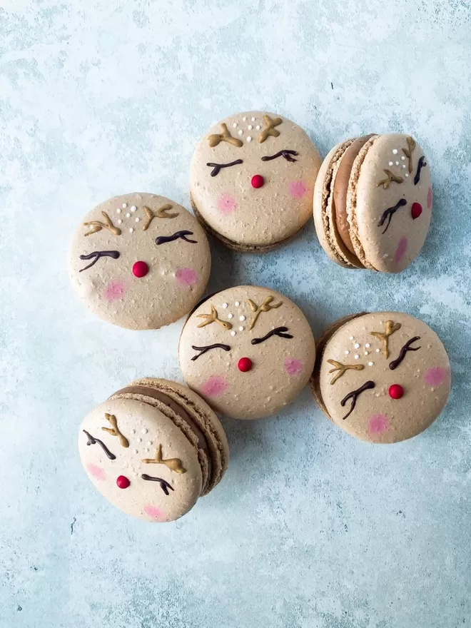 several macarons with reindeer faces painted on them with a red nose