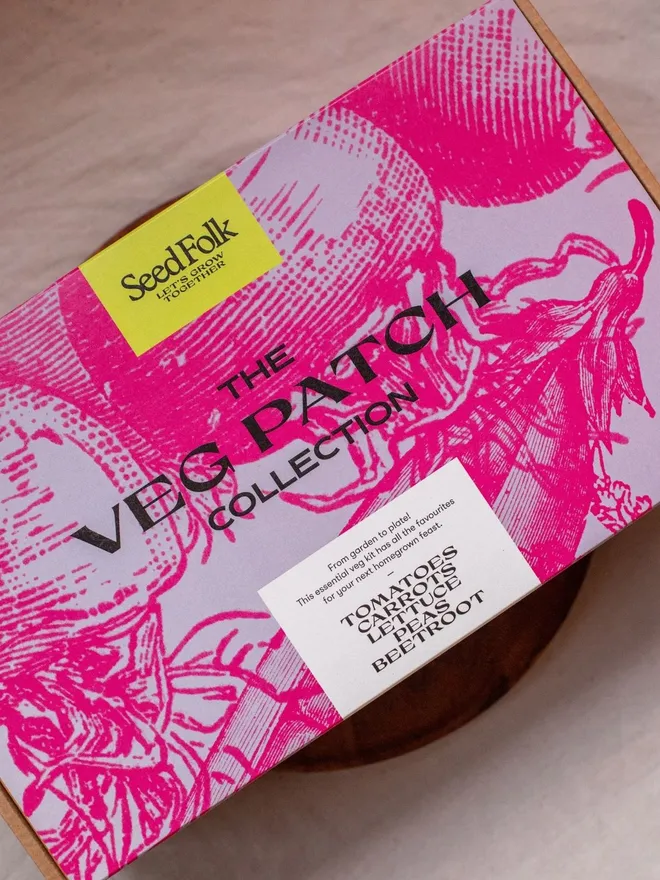 the Veg Patch seed starter kit. cardboard box in a pink decorative sleeve photographed on a wooden dish.