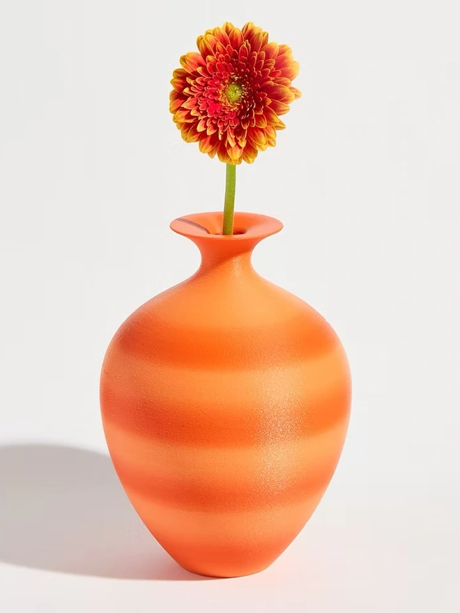 urn shaped bright orange 3d printed vase holding orange flower
