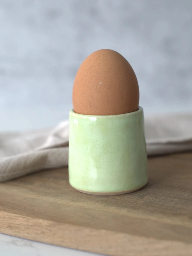 Classic Handmade Egg Cup, a ceramic egg cup sitting on a wooden chopping board against a grey backdrop. 